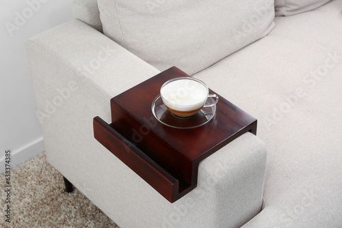 Cup of coffee on sofa with wooden armrest table indoors. Interior element photo