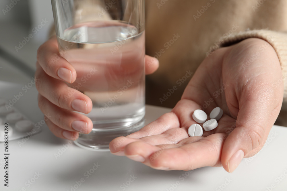 Woman with glass of water and pills at white table, closeup Woman with glass of water and pills at white table, closeup