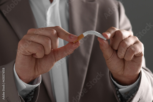 Stop smoking concept. Man breaking cigarette on gray background, closeup