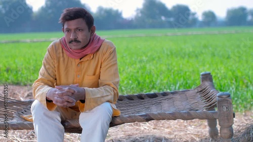 A mid-aged Indian villager sits alone on the Chaarpai - looking towards the camera. An Indian farmer wearing a Kurta-Pyjama posing for the camera photo