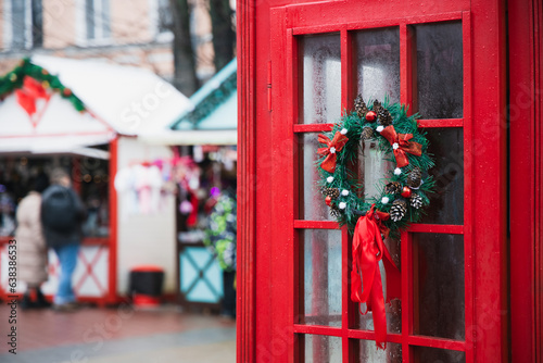 Christmas fair outdoor decoration festive atmosphere urban area with traditional British phone cabin red color foreground and blurred background people silhouette