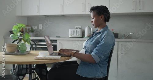 Pregnant woman working on laptop in kitchen photo