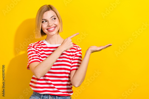 Photo of good mood gorgeous woman dressed striped t-shirt look at product empty space in arm isolated on vibrant yellow background