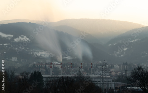 Smoke coming out of chimneys of heating plant at evening, Ponir mountain with sunlit top and glowing sky in background