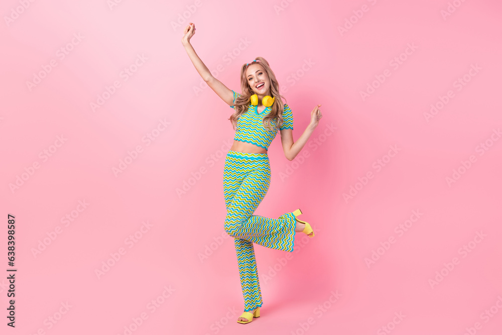 Full size photo of attractive young woman dancing raise hands headphones wear trendy green print clothes isolated on pink color background
