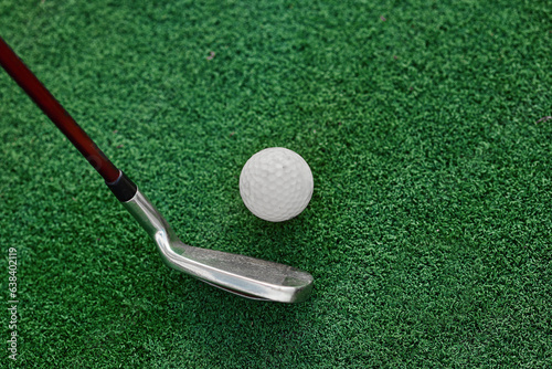 A vivid snapshot of a golf club, as a golfer focuses intensely on the ball resting atop the pristine artificial grass