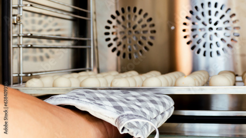 Heat-resistant gloves that are worn on the hand. holding a tray of many white round sweets Putting it in the baking oven Shot from a side angle, baking concept.
