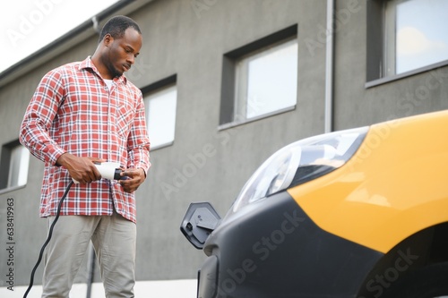 african man holding charge cable in on hand standing near electric car