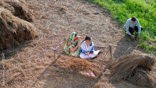 Mid-Aged Indian housewife braiding her daughter's hair while her husband works in the field - Beti Bachao Beti Padhao  village home  mother-daughter bonding  Indian family concept. Indian Desi moth... photo