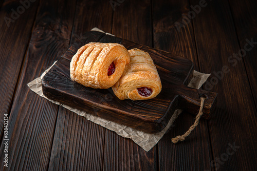 Bun from puff pastry with strawberry or cherry jam on brown boards. For decoration of bakery sales outlets. Bakery products. Fresh bakery.