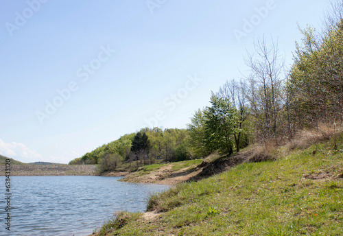 Beautiful lakeside view from a small lake in Serbia, with lush green trees, blue sky and sunlight