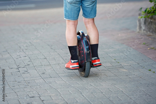 Man travel on mono wheel. Electric unicycle (EUC), personal mobility. Man in shorts rides on electric mono wheel down the city street in summer season. Man cycling on monowheel photo