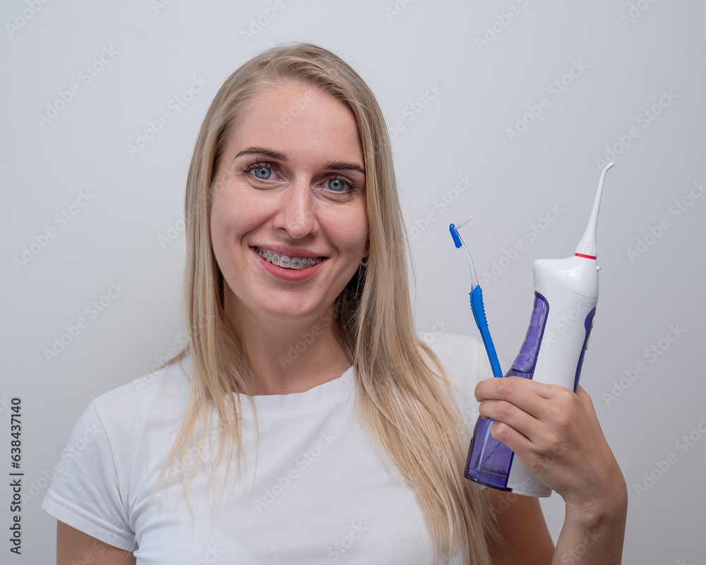 Smiling caucasian woman with braces on her teeth holding an irrigator and a toothbrush. Smiling caucasian woman with braces on her teeth holding an irrigator and a toothbrush.