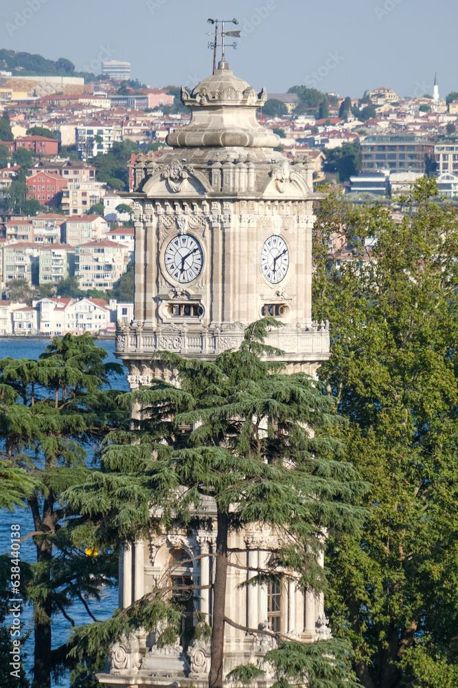 Dolmabahçe Palace clock tower with blue sky background, trees, buildings and sea. Open space area.