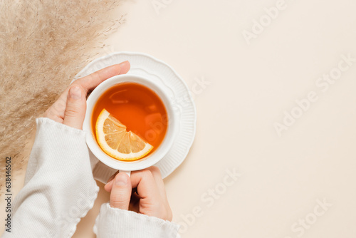 Woman hands hold cup of tea with lemon, pampas grass on beige background, copy space. Woman with cup of tea, cozy atmosphere, aesthetic minimal style. Autumn and winter theme