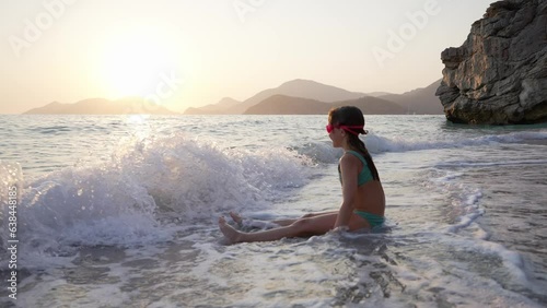 A Child Girl in a Swimsuit and Swimming Glasses Plays on the Sea Beach 