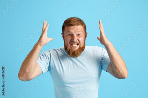 Photography Bearded redhead man emotionally shouting, expressing anger and irritation against blue studio background