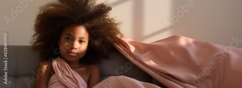 A pretty young girl is relaxing on a couch. Under a sheet. Curly hair. Sun through the window. Lazy day, childhood, after school memories.