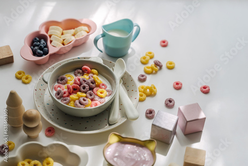 Dry children's breakfast. Cute children's plates and bowl with colorful cereal rings of milk. Creative serving for baby. Mess on the dining table. Concept of kids menu, nutrition and feeding.