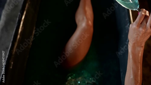 sexy lady relaxing in bath, pouring champagne into water, slender tanned legs and hand with glass