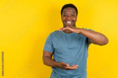 Young handsome man standing over yellow studio background gesturing with hands showing big and large size sign, measure symbol. Smiling looking at the camera. photo