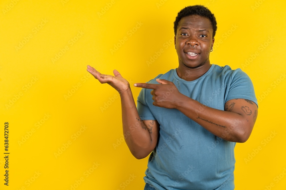 Young handsome man standing over yellow studio background pointing and holding hand showing adverts - obrazy, fototapety, plakaty 