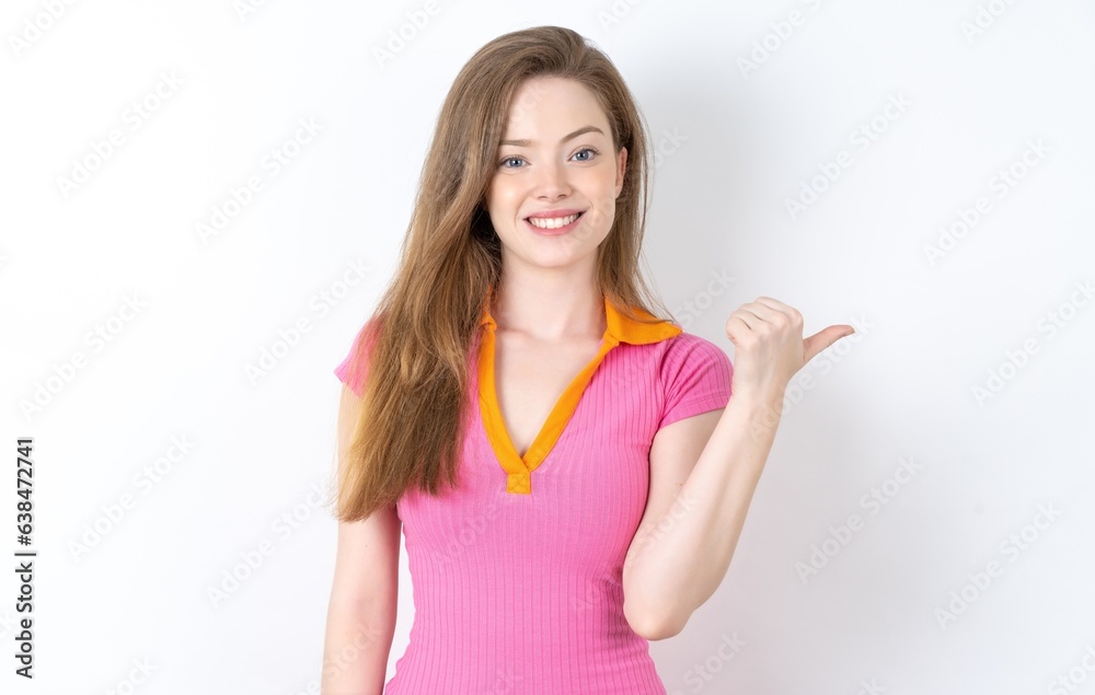 Lovely young beautiful red haired woman wearing pink dress pointing aside with forefinger, showing at copy space having news about bargains Lovely young beautiful red haired woman wearing pink dress pointing aside with forefinger, showing at copy space having news about bargains