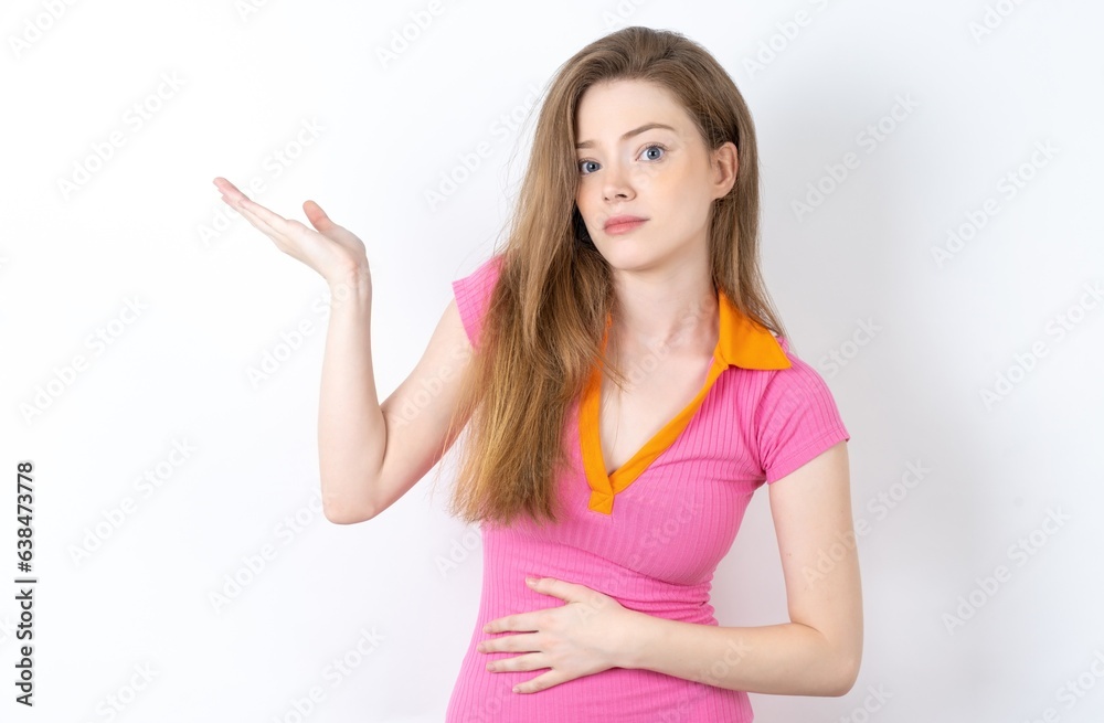 young beautiful red haired woman wearing pink dress pointing aside with both hands showing something strange and saying: I don't know what is this. Advertisement concept. young beautiful red haired woman wearing pink dress pointing aside with both hands showing something strange and saying: I don't know what is this. Advertisement concept.
