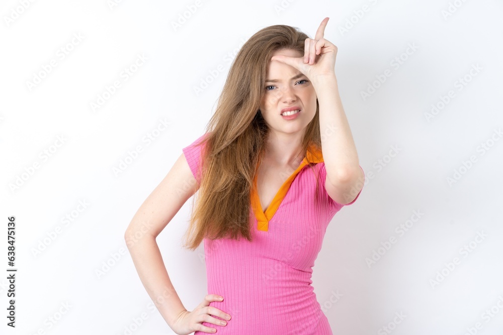 young beautiful red haired woman making fun of people with fingers on forehead doing loser gesture mocking and insulting. young beautiful red haired woman making fun of people with fingers on forehead doing loser gesture mocking and insulting.
