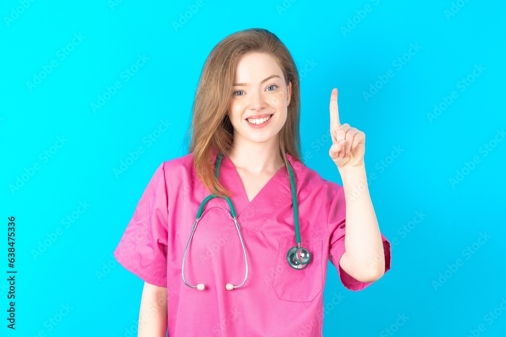 young beautiful red haired doctor woman showing and pointing up with finger number one while smiling confident and happy. young beautiful red haired doctor woman showing and pointing up with finger number one while smiling confident and happy.