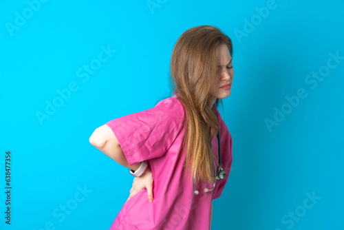 Beautiful doctor woman wearing pink medical uniform over blue background Suffering of backache, touching back with hand, muscular pain photo