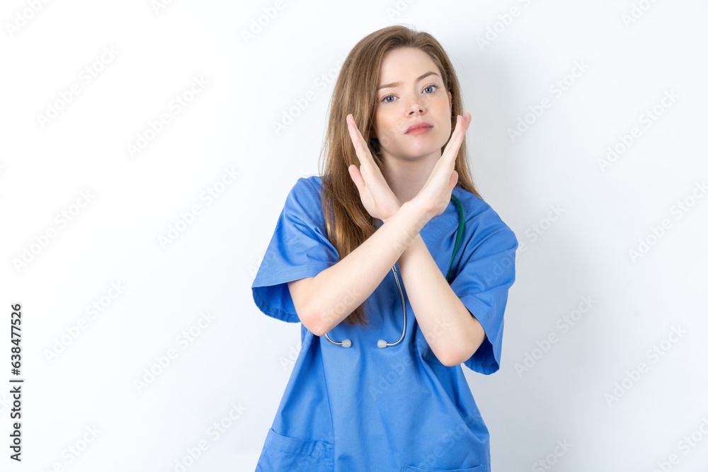 Beautiful doctor woman wearing blue medical uniform over blue background Rejection expression crossing arms doing negative sign, angry face Beautiful doctor woman wearing blue medical uniform over blue background Rejection expression crossing arms doing negative sign, angry face