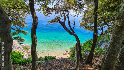 Fototapeta Naklejka Na Ścianę i Meble -  A view on the seashore from a cliff above the beach in Croatia. The sea has turquoise color and is very clean. There are a few trees growing on the steep cliffs. Stony beach. Sunny and warm day.