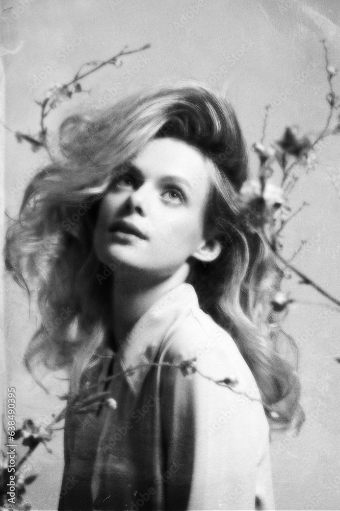 Woman with big wavy hair studio portrait. Model surrounded with flower twigs with blossoms. Retro vintage style with grain, noise, blur and grunge texture effect applied. Black and white image Woman with big wavy hair studio portrait. Model surrounded with flower twigs with blossoms. Retro vintage style with grain, noise, blur and grunge texture effect applied. Black and white image