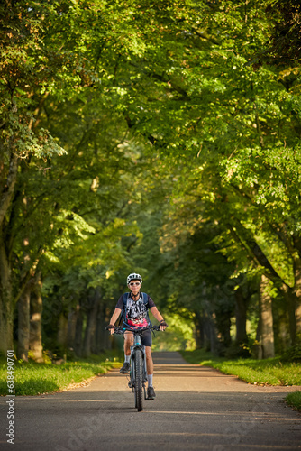 Wallpaper Mural attractive senior woman cycling with her electric mountain bike in a beautiful old oak tree and chestnut avenue in Ludwigsburg, Baden-Wuerttemberg, Germany
 Torontodigital.ca