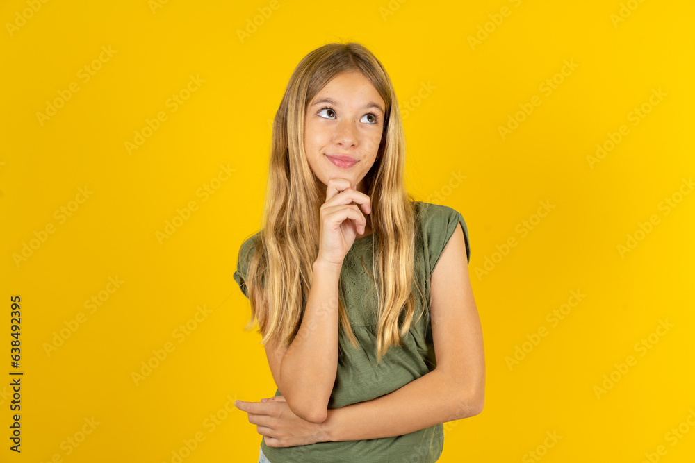 Thoughtful Beautiful caucasian kid girl wearing green dress holds chin and looks away pensively makes up great plan Thoughtful Beautiful caucasian kid girl wearing green dress holds chin and looks away pensively makes up great plan