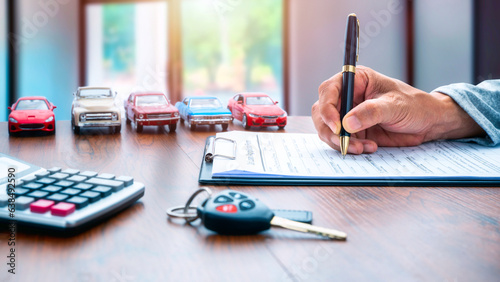 Man signing contract on car loan application form. Car loan or buying a new car concept. Miniature cars and car key on table.  © Boxyray