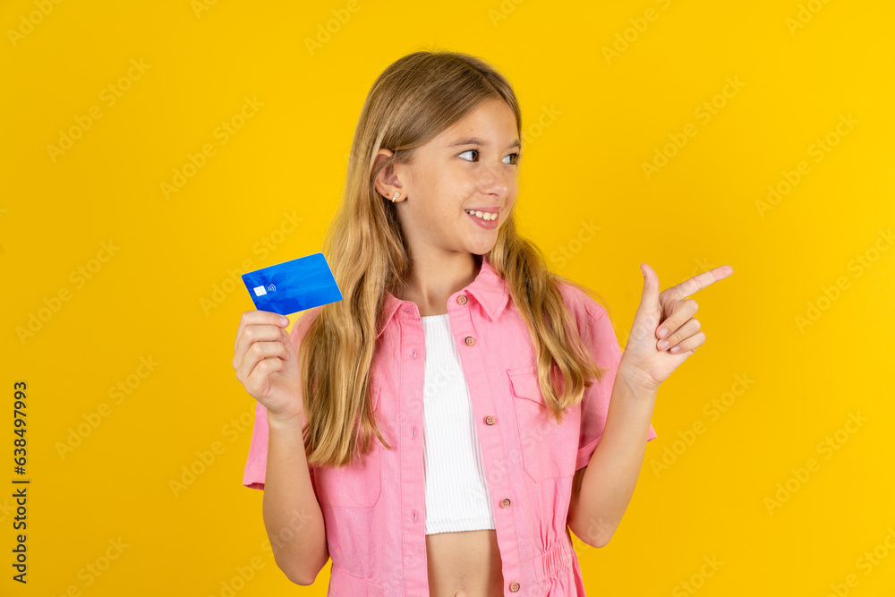 Curious smiling Beautiful caucasian kid girl wearing pink shirt showing plastic bank showing finger copyspace Curious smiling Beautiful caucasian kid girl wearing pink shirt showing plastic bank showing finger copyspace