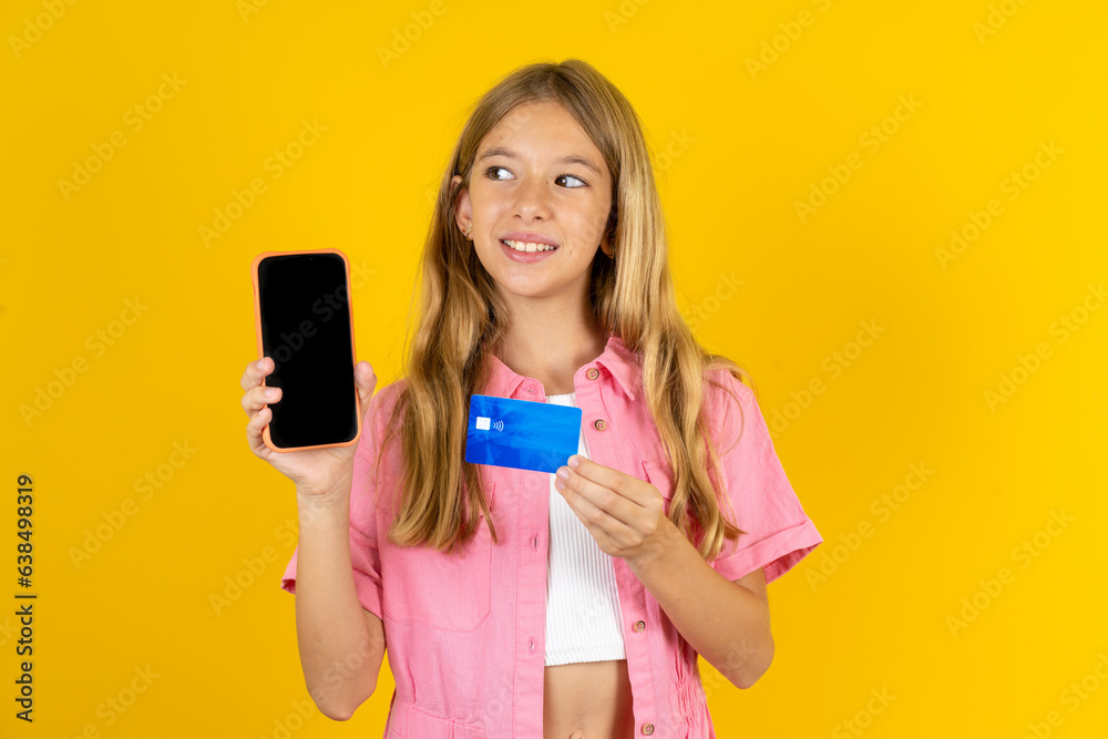 Beautiful caucasian kid girl wearing pink shirt holding bank card modern device looking empty space Beautiful caucasian kid girl wearing pink shirt holding bank card modern device looking empty space