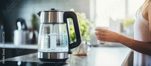 Water filter system in a kitchen with a woman s hand holding a modern electric kettle focused on the on and off button