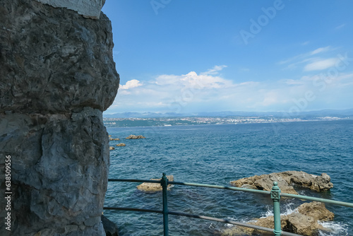 A panoramic view on the cities located along the coastal line of Istria, Croatia. There is a steep stone wall on the side and a pathway along it. The Mediterranean Sea is calm. Clear and sunny day. photo