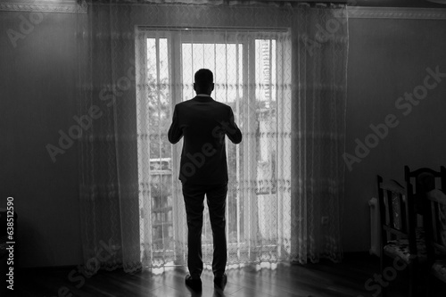 A man in a classic suit is standing by the window. A guy in trousers and a jacket looks out the window