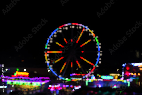 modern ferris wheel with closed cabins at carnival with blue sky no clouds in the background illuminated wide angle close up shot