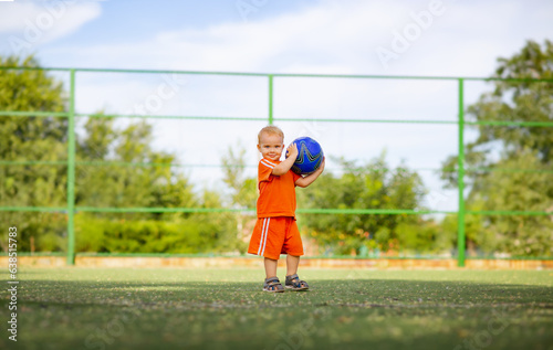 little blond boy posing with ball, child walking on playground on nature, active summer leisure and sport concept
