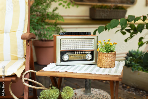 The FM channel is playing music, a stylish retro radio player stands on a wooden table. Close up view of beautiful vintage radio and flowers in pot. 