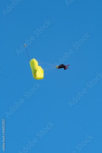 Obraz na płótnie Stunning view of of a skydiver with a yellow parachute and a blue sky in the background w salonie
