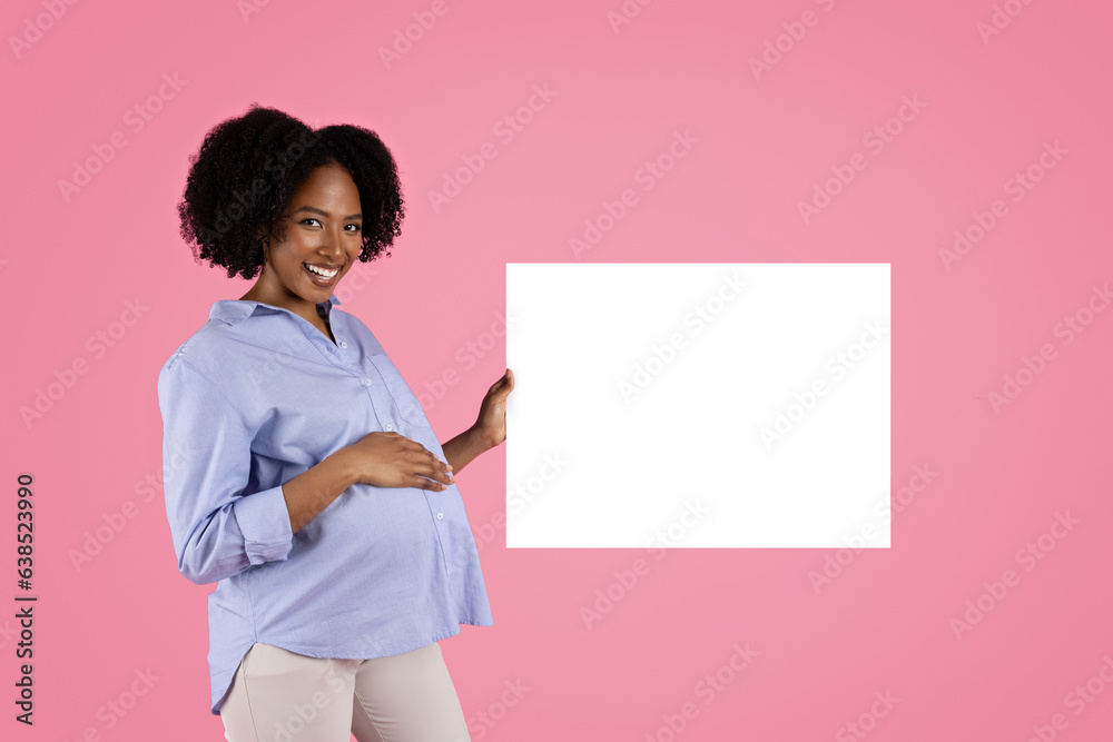 Glad young black pregnant lady in casual touching big belly, enjoy motherhood showing banner with blank space Glad young black pregnant lady in casual touching big belly, enjoy motherhood showing banner with blank space