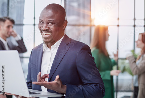 Young african american man in business suit holding laptop while standing at office corridor