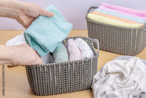 Women's hands fold clean clothes. Vertical storage of clothing in the baskets. Closet cleaning