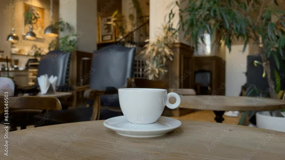 A cup of hot black steaming coffee on a wooden table, atmosphere of a cafe or coffee shop in the bokeh background A cup of hot black steaming coffee on a wooden table, atmosphere of a cafe or coffee shop in the bokeh background